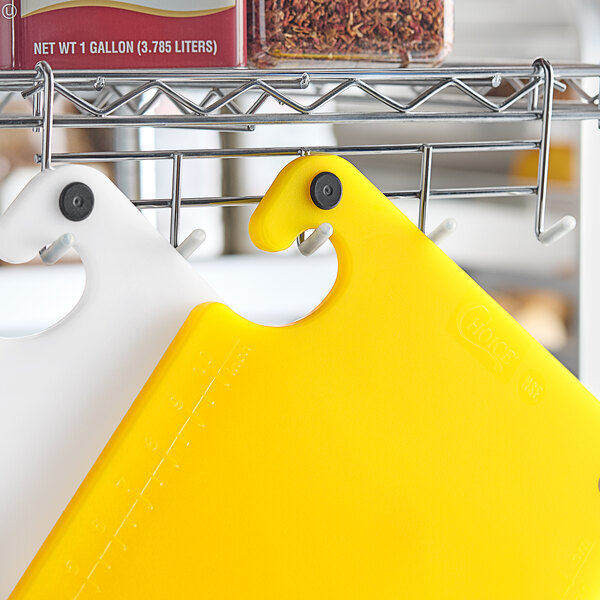 A yellow cutting board with white grips and rulers on a metal shelf.