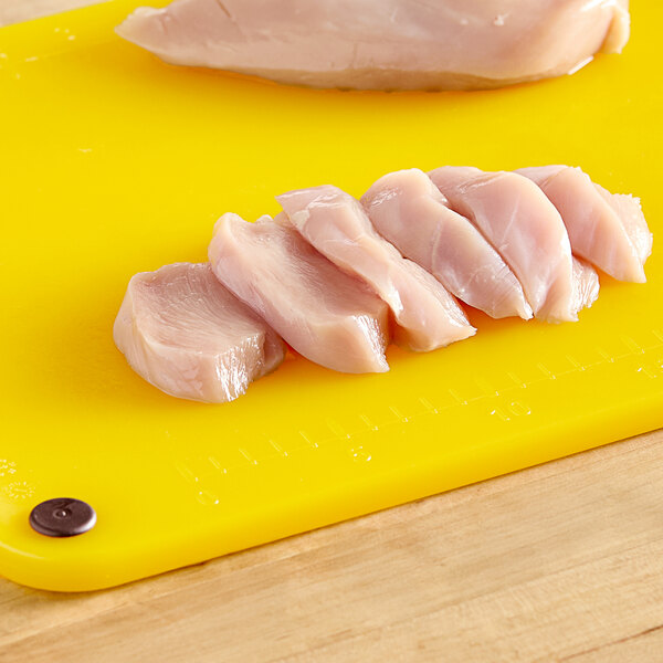 A group of raw chicken meat on a yellow Choice cutting board with rulers and grips.