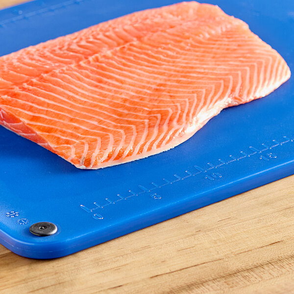 A piece of salmon on a blue cutting board with rulers and grips.