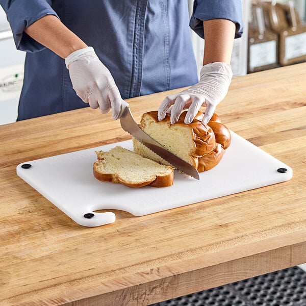 A woman using a Choice white cutting board to cut a loaf of bread.