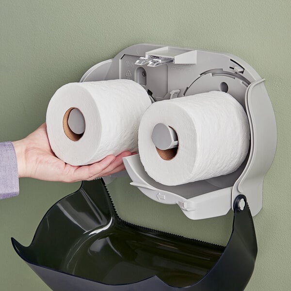 A hand holding an individually wrapped Tork standard toilet paper roll.