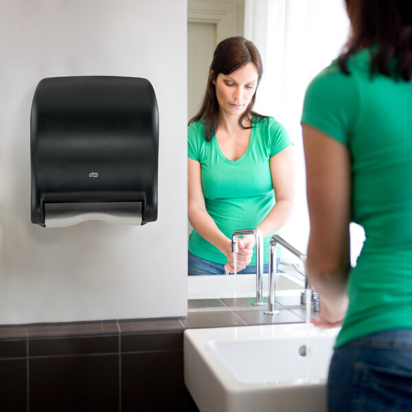 A black electronic touch-free automatic hand towel dispenser mounted on a restroom wall.