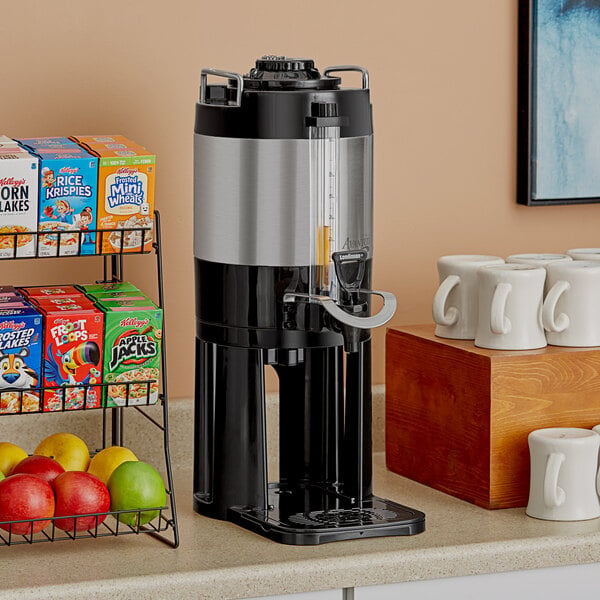 An Avantco coffee maker on a counter with a white thermal server next to fruit baskets.