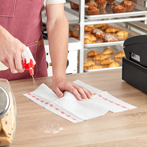 A person using a Tork white and red striped food service wiper to clean a table.