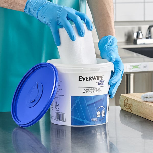A person in blue gloves putting a roll of Everwipe paper in a blue Everwipe bucket.