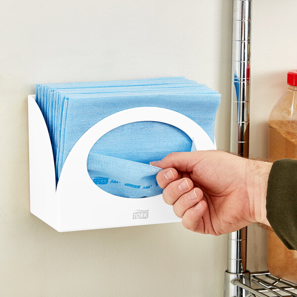 A hand holding a blue plastic Tork wiper dispenser.