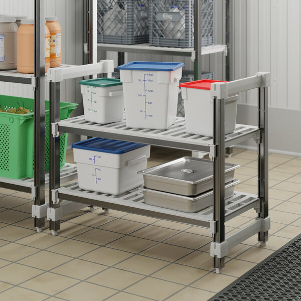 A white and blue Cambro Camshelving unit with a silver metal shelf and white and green containers on it.