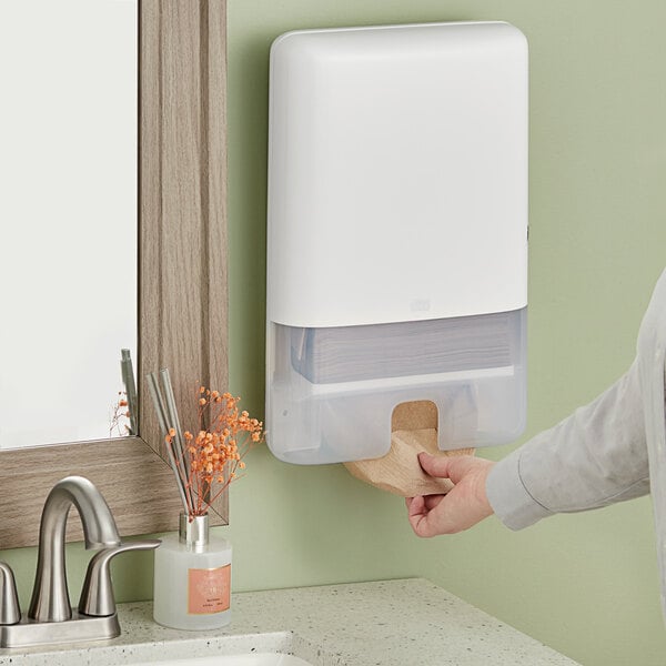 A woman using a white Tork wall mount multifold hand towel dispenser.