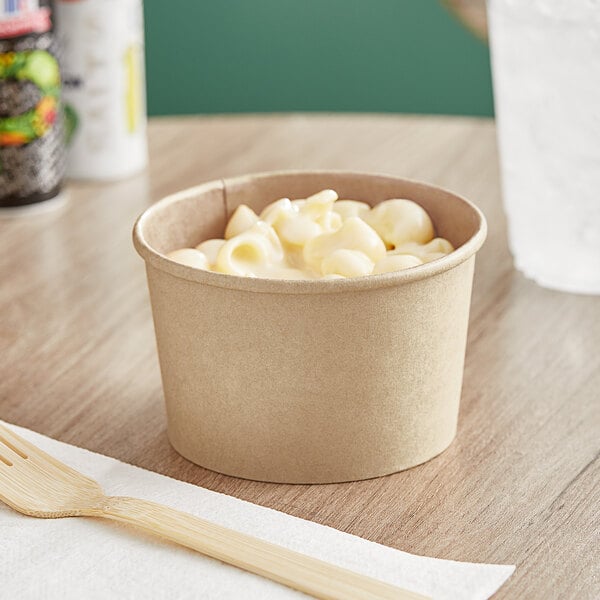 A Choice paper food cup filled with macaroni and cheese on a table.