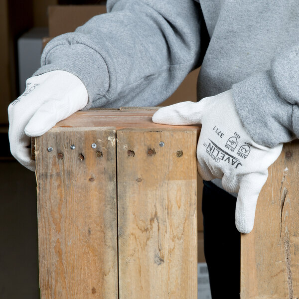 A pair of white HPPE and synthetic fiber gloves with a white polyurethane palm coating being worn by a person handling wooden boards.