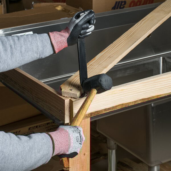 A person wearing Cordova Cut-Resistant gloves with black foam nitrile palms using a hammer to nail a piece of wood.