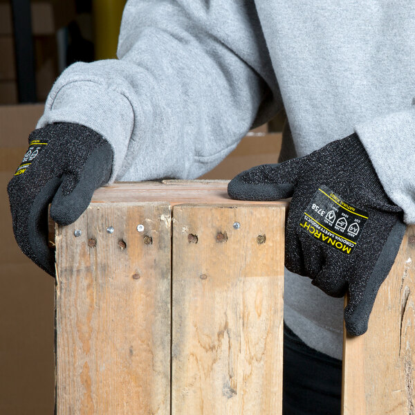 A person wearing Cordova Monarch black latex palm coated gloves holding a piece of wood.