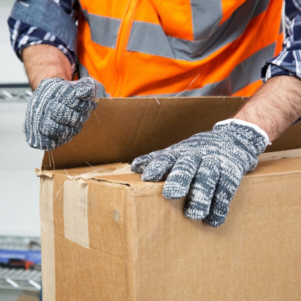 A person wearing Cordova multi-color work gloves holding a box.