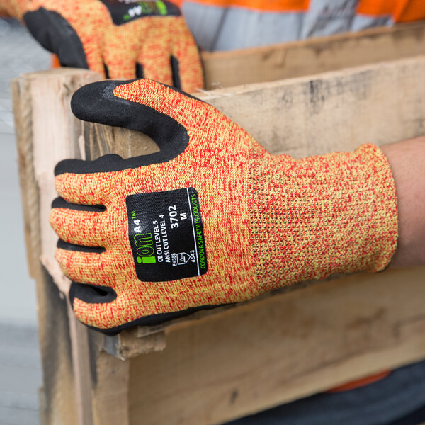 A person wearing small orange Cordova heavy duty work gloves with black sandy nitrile palms holding a piece of wood.