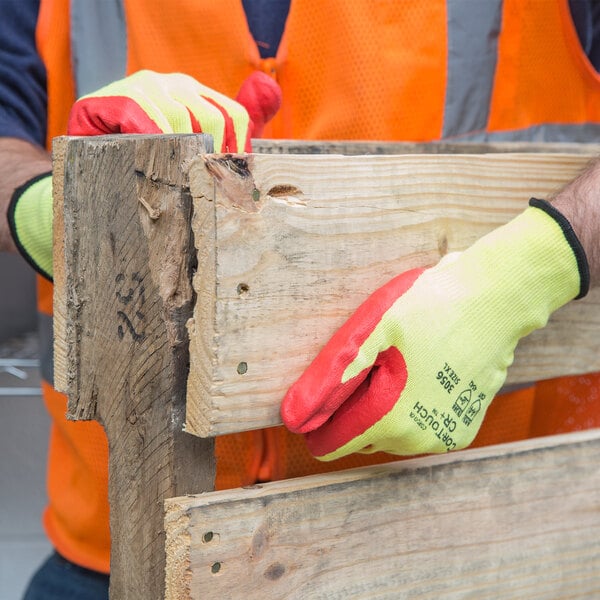 A person wearing a Cordova yellow cut-resistant glove holding a piece of wood.