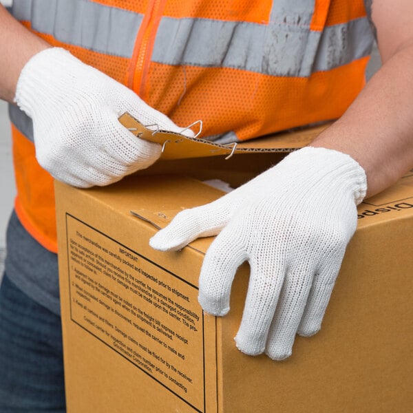 A pair of white polyester work gloves being worn by a person handling a cardboard box.