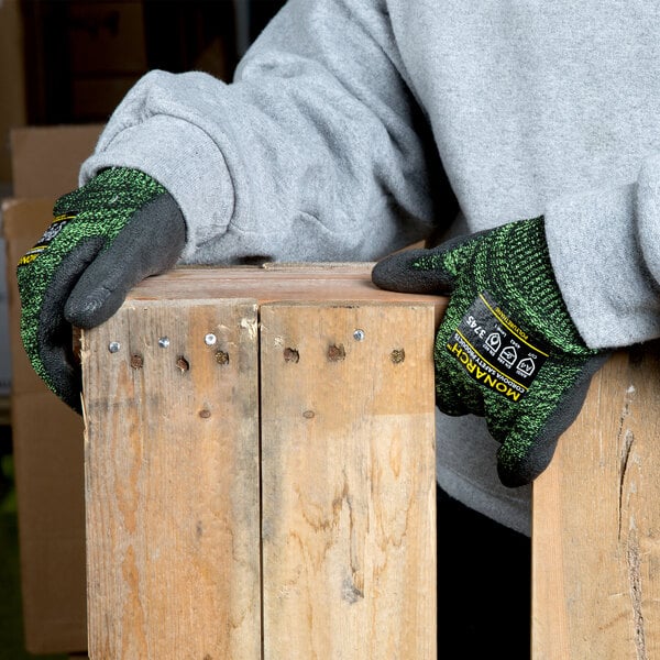 A person wearing Cordova Monarch Soft Green Cut-Resistant gloves with black palms leaning on a piece of wood.