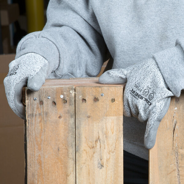 A person wearing Cordova Caliber gloves with gray polyurethane palms leaning on a piece of wood.