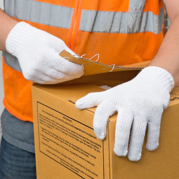 A person wearing Cordova standard weight white polyester/cotton work gloves holding a box.