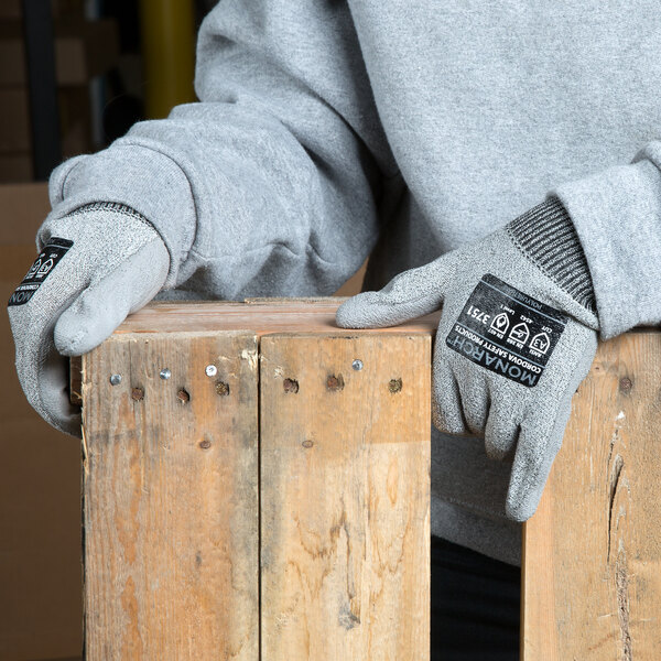 A person wearing Cordova Monarch gray cut-resistant gloves holding a piece of wood.