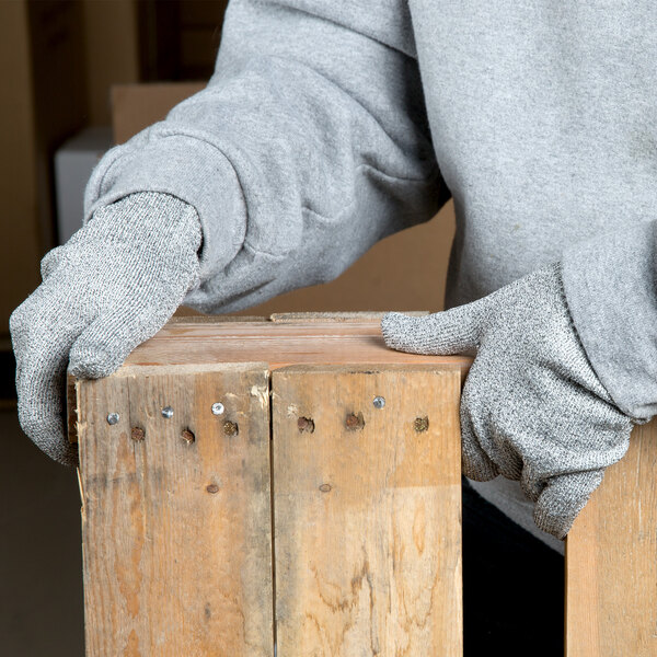 A person wearing Cordova Monarch gray engineered fiber cut-resistant gloves holds a wood plank.