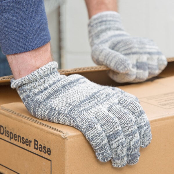 A person wearing Cordova medium weight multi-color jersey gloves holding a box.