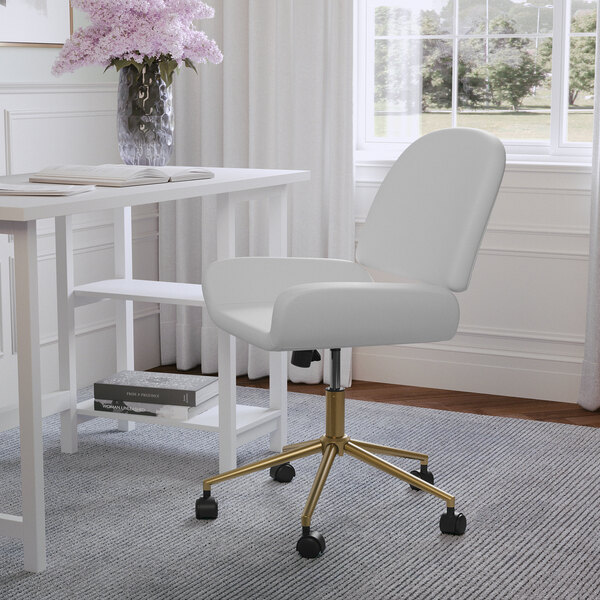 A Martha Stewart white faux leather swivel office chair with a gold base in front of a window.