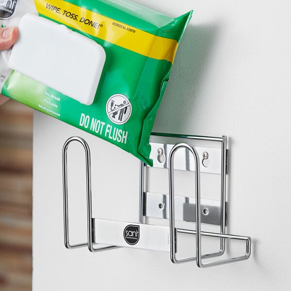 A hand holding a white plastic wall mount bracket for Sani Professional soft pack wipes.