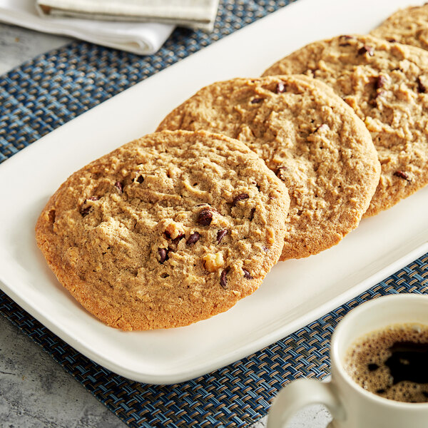 Pre-formed Michael's vegan chocolate chip walnut cookies on a plate with a cup of coffee.