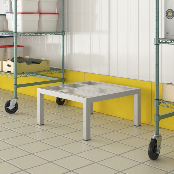 A Regency aluminum dunnage rack on a white tile floor next to a yellow cart.