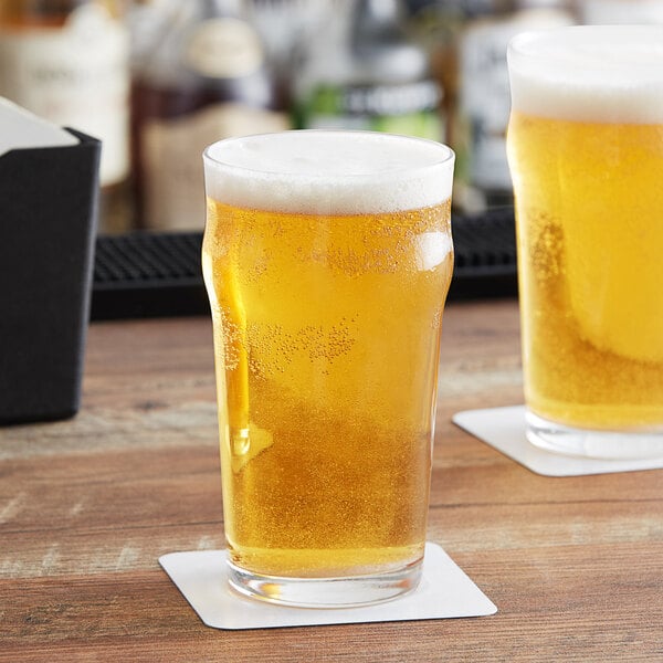 Two Acopa Select English Pub glasses of beer on a wooden table.