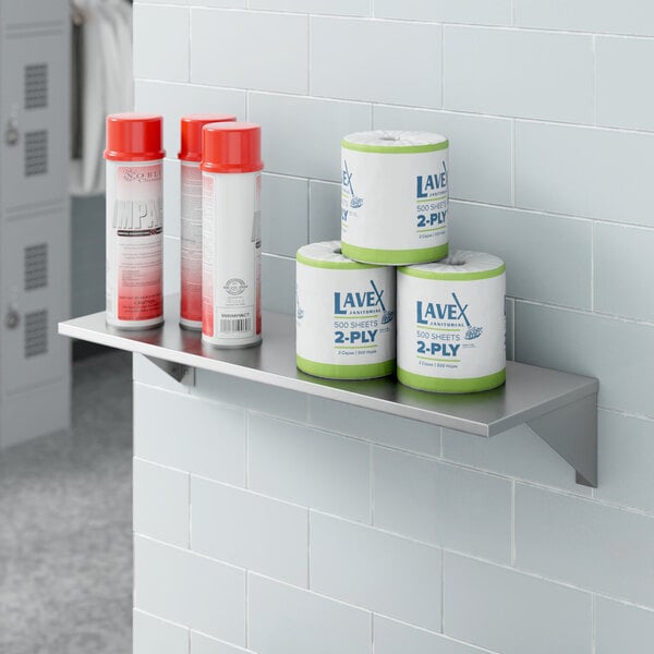 A Lavex stainless steel wall mount shelf with cans on it.