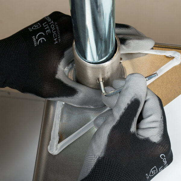 A person in Cordova black nylon gloves with gray polyurethane palm coating fixing a metal pipe.