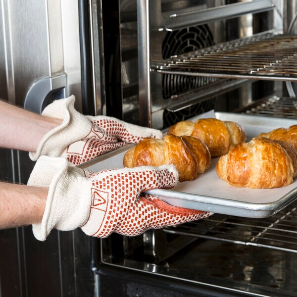 A person using Cordova hot mill gloves to hold a tray of croissants in an oven.