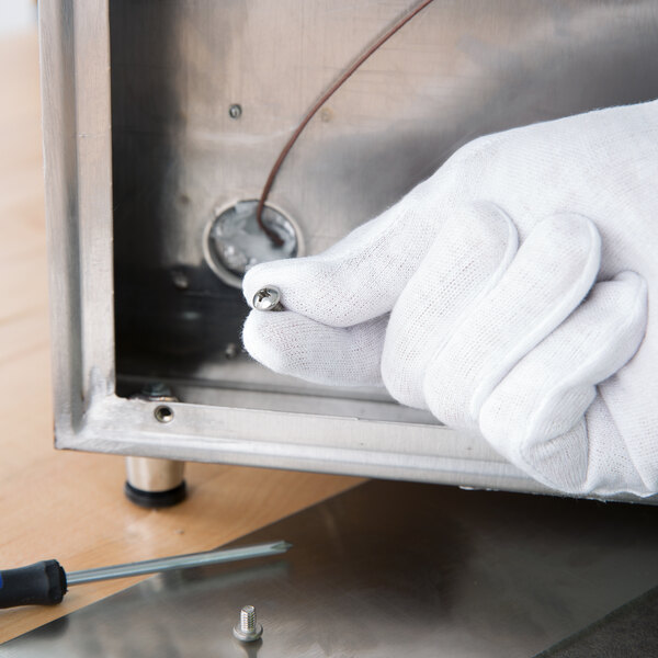 A person wearing a white Cordova inspection glove using a screwdriver on a table.