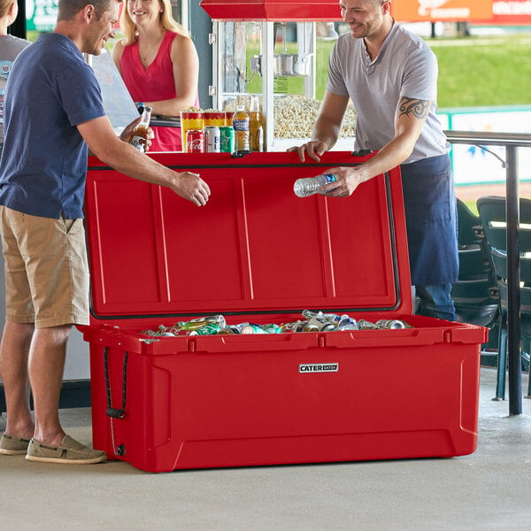 Two men standing next to a red CaterGator outdoor cooler with the lid full of cans.