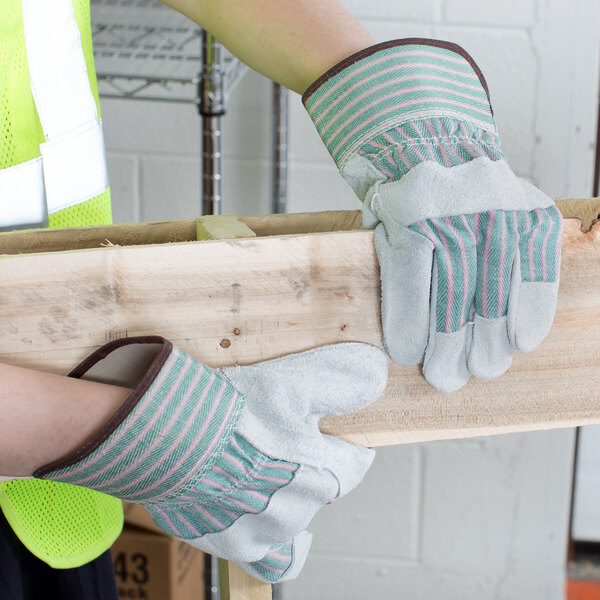 A person wearing small Cordova striped canvas work gloves with leather palms holding a piece of wood.