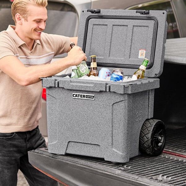 A man opening a CaterGator outdoor cooler filled with green bottles.