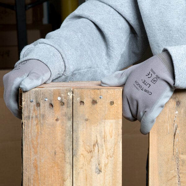 A person wearing Cordova gray nylon gloves holding a piece of wood.