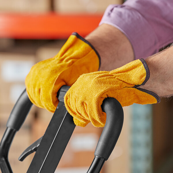 A person wearing Cordova Russet Select Split Cowhide Leather driver's gloves holding a tool in a warehouse.
