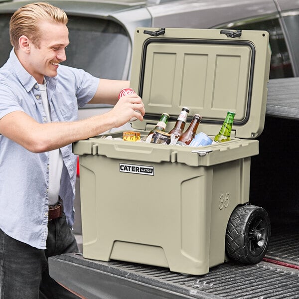 A man putting bottles in a CaterGator tan outdoor cooler.