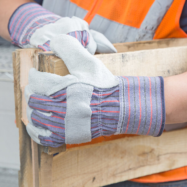 A person wearing Cordova striped canvas work gloves with leather palms and rubber cuffs holding a piece of wood.