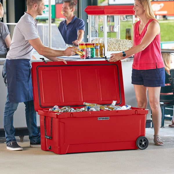 A man and a woman standing next to a red CaterGator outdoor cooler with the lid open.