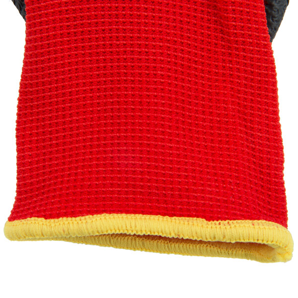 A close-up of a red and yellow knitted fabric glove with dark gray latex coating on the palm.