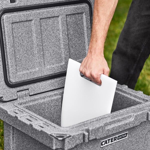 A hand placing a white CaterGator divider in a grey cooler.