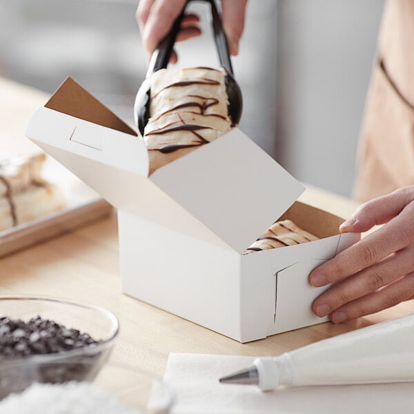 A person putting a piece of cake into a white bakery box.