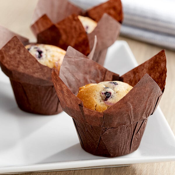 Three Baker's Mark chocolate brown large muffins in brown paper cups on a white plate.