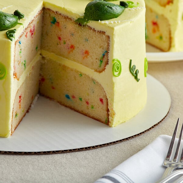 A Baker's Mark white cake circle with a slice of cake with colorful sprinkles on top.
