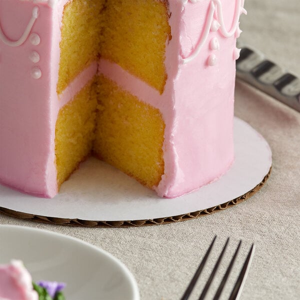 A Baker's Mark white cake circle with a slice of cake on a plate.