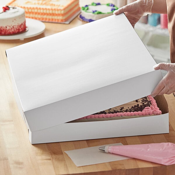 A person holding a white Baker's Mark full sheet cake box.